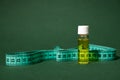 Still life with a glass vial of massage anti cellulite oil and measure tape, isolated on green background Royalty Free Stock Photo