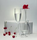 Still life of a glass of water and two empty glasses with a rose and cherries on a white background Royalty Free Stock Photo