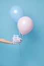 Hand holding stack of ironed laundered newborn baby clothes and booties, blue and pink balloons, isolated blue backdrop Royalty Free Stock Photo