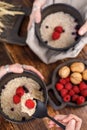 Still life with hands that hold exquisite ceramic bowls with oatmeal and fresh raspberries on a wooden backgroun.