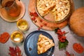 Still life: Homemade pumpkin pie with apples, crispy crust, and cups of hot tea, surrounded by autumnal fallen leaves.