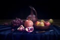 Still life with a jug of wine, pomegranate, red grapes, apples and pears on a dark blue linen tablecloth on a black background. Royalty Free Stock Photo