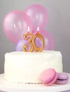 Still life: a lit candle with the number 30 on a white cake with macaroni cakes and pink balls with a place for text, birthday