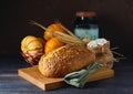 Still life with a loaf of pumpkin bread, spikelets, decorative pumpkins and a wooden board. World Bread Day