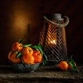 Still life with mandarins in the tin bowl and candlelight on wooden background