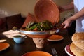 Housewife serving delicious meal with steamed vegetables, cooked in clay pot according to traditional Moroccan recipe.