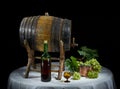 Still life with old oak wine barrel, wine bottle, wine glass and bronze container with bunch of grapes on black background Royalty Free Stock Photo