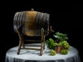Still life with old oak wine barrel, and bronze container with bunch of grapes on black background Royalty Free Stock Photo