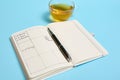 Still life of an open agenda with schedule, ink pen and transparent glass cup of tea lie on blue surface. Color background with Royalty Free Stock Photo