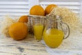 Still life with oranges, basket and glass jug with juice on old bright wooden background