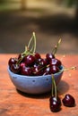 Still life of a pair of fresh ripe cherries on rustic wooden table against a blue ceramic bowl full of summer berries