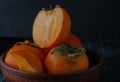 Still life with persimmon on a plate on a dark background.