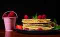 Still life. A plate of pancakes with fresh berries and mint leaves near a bucket with strawberries over dark background. Royalty Free Stock Photo