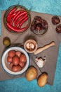 Still life with a plate of raw eggs, raw potatoes, garlic in a wooden mortar, dried peppers and red chili peppers on gray cloth