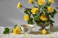 Still-life with porcelain cup of coffee, yellow garden rose flowers on pin frog in vintage vase on white lace tablecloth Royalty Free Stock Photo