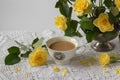 Still-life with porcelain cup of coffee, yellow garden rose flowers on pin frog in vintage vase on white lace tablecloth Royalty Free Stock Photo