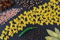 Still life with raw farfalle, different spices and salt on a black stone serving board. Italian uncooked pasta. Food concept or Royalty Free Stock Photo