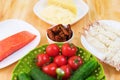 Still life of raw food in white plates on a wooden table. Frozen salmon on a plate next to cucumbers and tomatoes grated