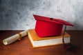 Still life with a red graduation hat on a book next to a diploma on a wooden desk. Graduation and studies concept