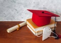 Still life with a red graduation hat on books next to a diploma and a mask on a wooden desk