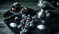 Still life in royal style. Frozen berry of blackberry with silver sugar bowl and spoon on black stone