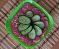 still life, sausage, cucumbers, in a green square plate, on a striped brown background, original picture
