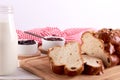 Still life with string of Christmas cake or sweet pastry with raisins and almond slices, glass of milk and bowls with fruit jam. Royalty Free Stock Photo