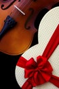 Close up of a classic violin and a heart shape gift box with a red ribbon bow Royalty Free Stock Photo