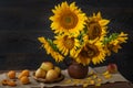 Still life with sunflowers in a clay pot and fruit on against a wooden wall