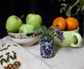Still life of tangerines , three green aples and vase of purple flower