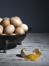 Still life with a tin bowl full of a pile of eggs and a broken egg on a white table with a blue background Royalty Free Stock Photo
