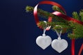 Still life for Valentine`s day two silver hearts on a coniferous branch with a red ribbon on a dark blue background,