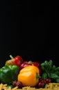 Still life of vegetables, colored peppers, tomato, basil and pasta on a dark background Royalty Free Stock Photo
