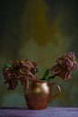 still life of wilted flowers in a copper vase, on a wooden table, against an abstract warm background of a textured wall Royalty Free Stock Photo