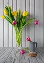 Still life yellow pink white tulips,glass vase,green leaves,flower in cast-iron steel jug,on table,wood board,copy space Royalty Free Stock Photo