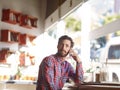 Are we still on for our coffee date. a young man talking on his cellphone while sitting in a cafe. Royalty Free Stock Photo