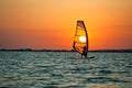 Still sea surface, man practicing wind surfing and golden sunset in sky Royalty Free Stock Photo