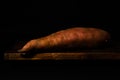 Stillife of a sweet potato on a wooden table against a dark background