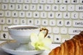 Stilllife of coffee cup with espresso, croissant or biscuit, flower and imitation of keyboard on a wooden background