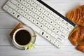 Stilllife of coffee cup with espresso, croissant, biscuit, flower and imitation of keyboard on a wooden background
