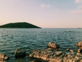 the stillness of the sea, the sunlight reflecting on the rocks and a green mountain in the distance