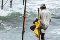 Stilt fisherman with his wooden rod facing back to the camera with his yellow pocket on the pole