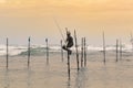 Stilt fisherman sitting in his pole with a wooden fishing rod in his hands in the sunset evening. Ocean waves crash behind him in Royalty Free Stock Photo