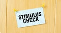 STIMULUS CHECK sign written on sticky note pinned on wooden wall