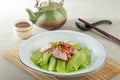 Stir-fried Chinese Lettuce with Sichuan Smoked Bacon Bits in a dish isolated on wooden mat side view on grey background