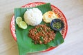 Stir-fried minced pork with basil leaves served with rice and fried egg on banana leaf on zinc tray over wooden table background Royalty Free Stock Photo