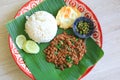 Stir-fried minced pork with basil leaves served with rice and fried egg on banana leaf on zinc tray over wooden table background. Royalty Free Stock Photo