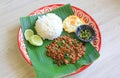 Stir-fried minced pork with basil leaves served with rice and fried egg on banana leaf on zinc tray over wooden table background Royalty Free Stock Photo