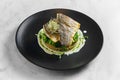 Stir-fried sea bass fillet with quinoa and broccoli garnish with creamy sauce, served in a black plate on a marble background. Royalty Free Stock Photo