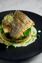 Stir-fried sea bass fillet with quinoa and broccoli garnish with creamy sauce, served in a black plate on a marble background. Royalty Free Stock Photo